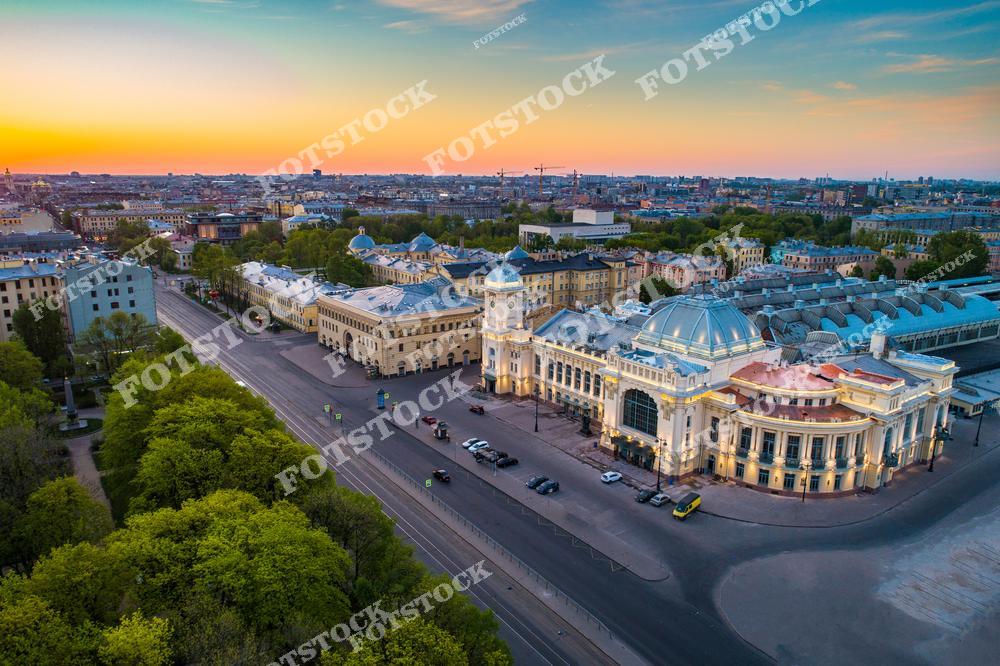 Панорамная фотография Санкт-Петербурга с высоты птичьего полета, на которой запечатлен Витебский вокзал, железнодорожные пути и улицы исторического центра города. Съемка с дрона позволяет увидеть масштаб транспортной инфраструктуры, архитектуру старейшего вокзала России и панораму городской застройки Северной столицы. Фотография передает атмосферу современного мегаполиса с богатым историческим наследием, сочетая железнодорожные линии, городские улицы и архитектурные ансамбли Петербурга. Снимок идеально подходит для туристических публикаций, фотостоков, рекламы, оформления интерьеров и материалов о транспорте и достопримечательностях Санкт-Петербурга.